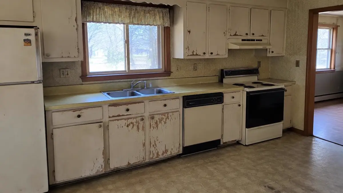 Dated kitchen with worn cabinets and old appliances in a house sold as-is