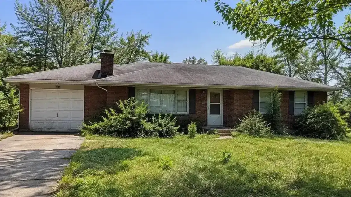 Older brick ranch house with an overgrown yard