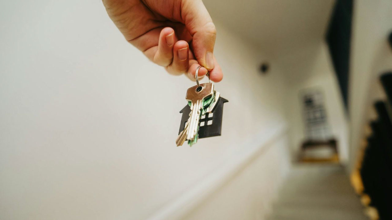 Hand holding house keys with a home-shaped keychain, symbolizing the process to sale your house by own.